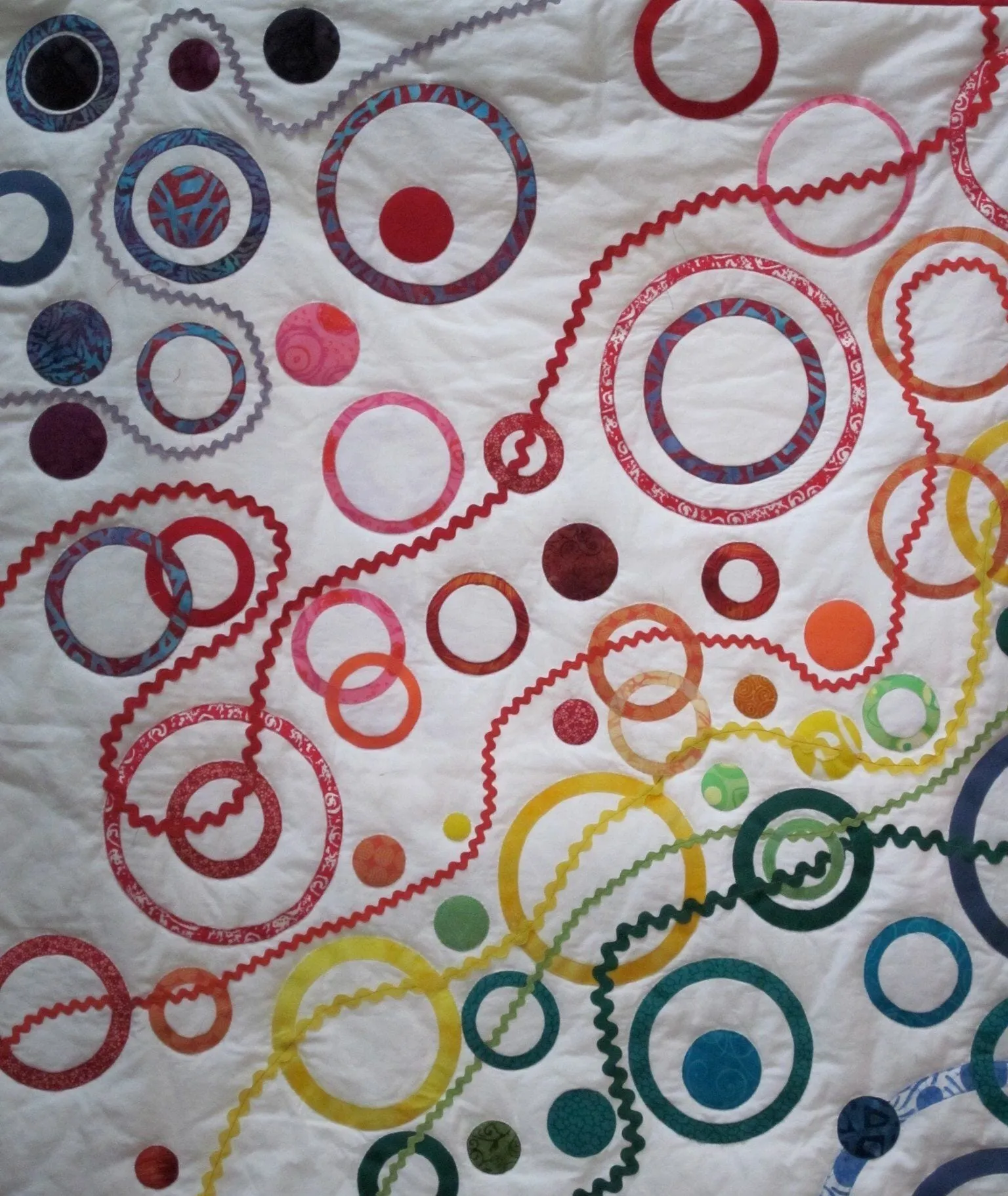 A baby quilt quilted with concentric circles in many colors on white, the rings overlapping and running off the edges.