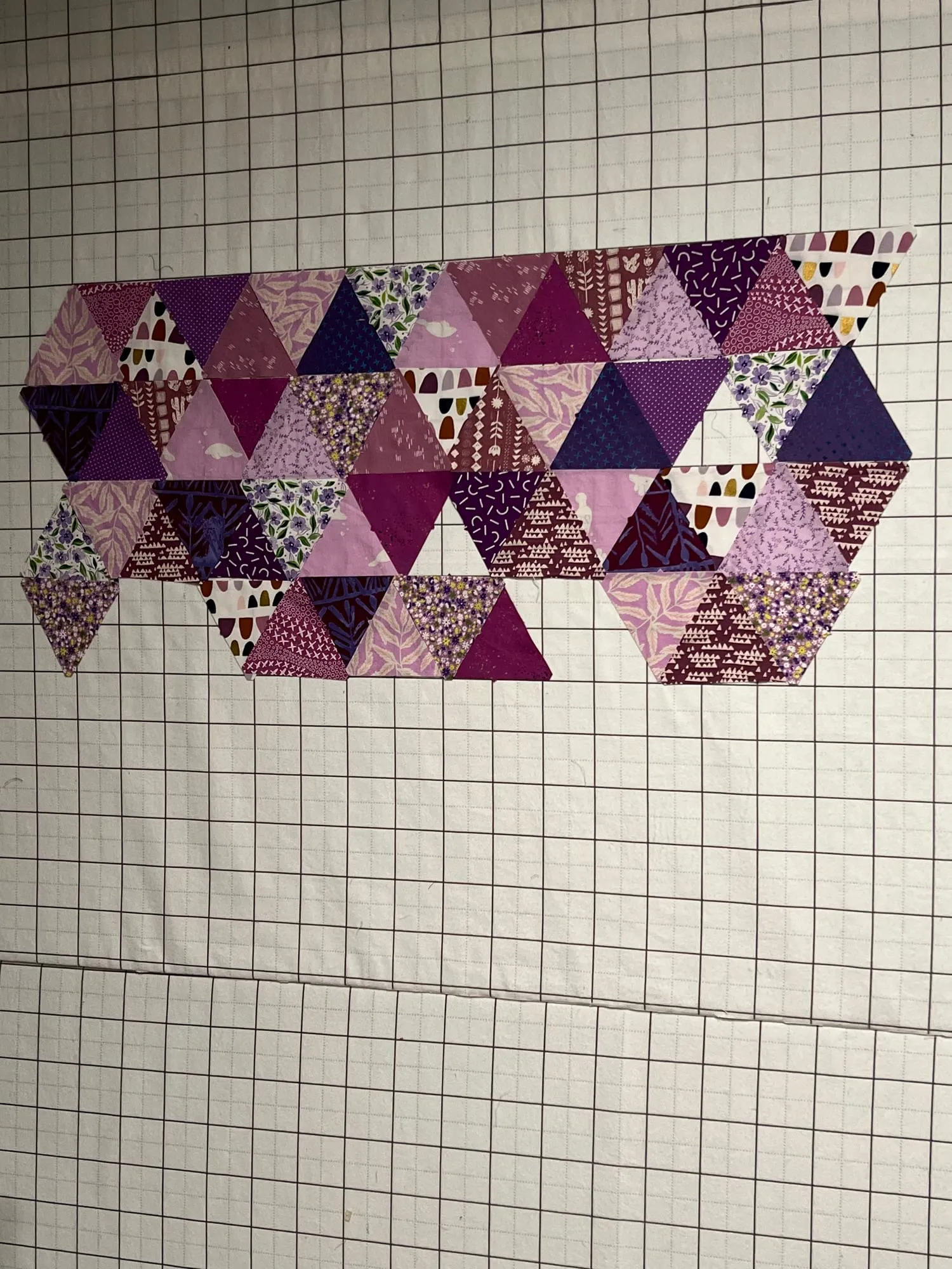 Pieced triangles in purples and pinks laid out in rows on a gridded cutting mat, working out the arrangement before sewing.
