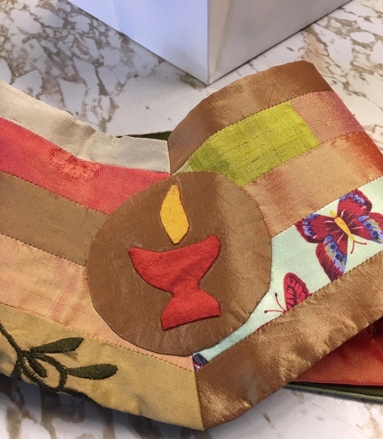 The back of an ordination stole, hand appliquéd in silk: a chalice and flame on a circle, with a butterfly and bands of gold, red and green.