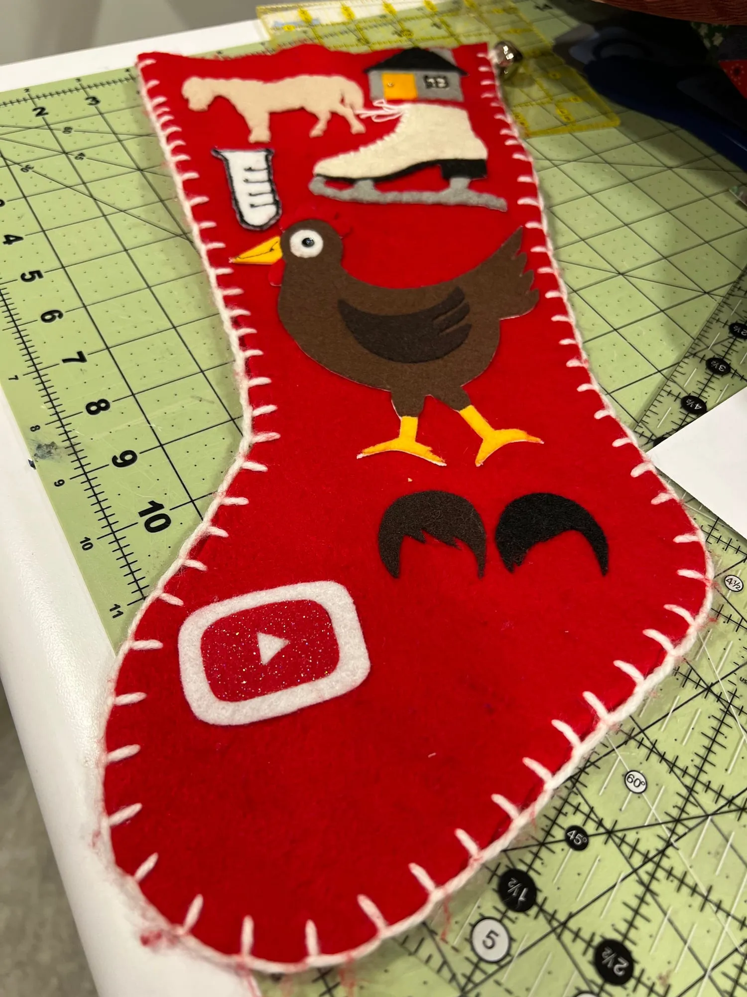 The back of the same stocking, with a pale horse, a white ice skate, a brown hen with yellow feet and beak, and a video play button.
