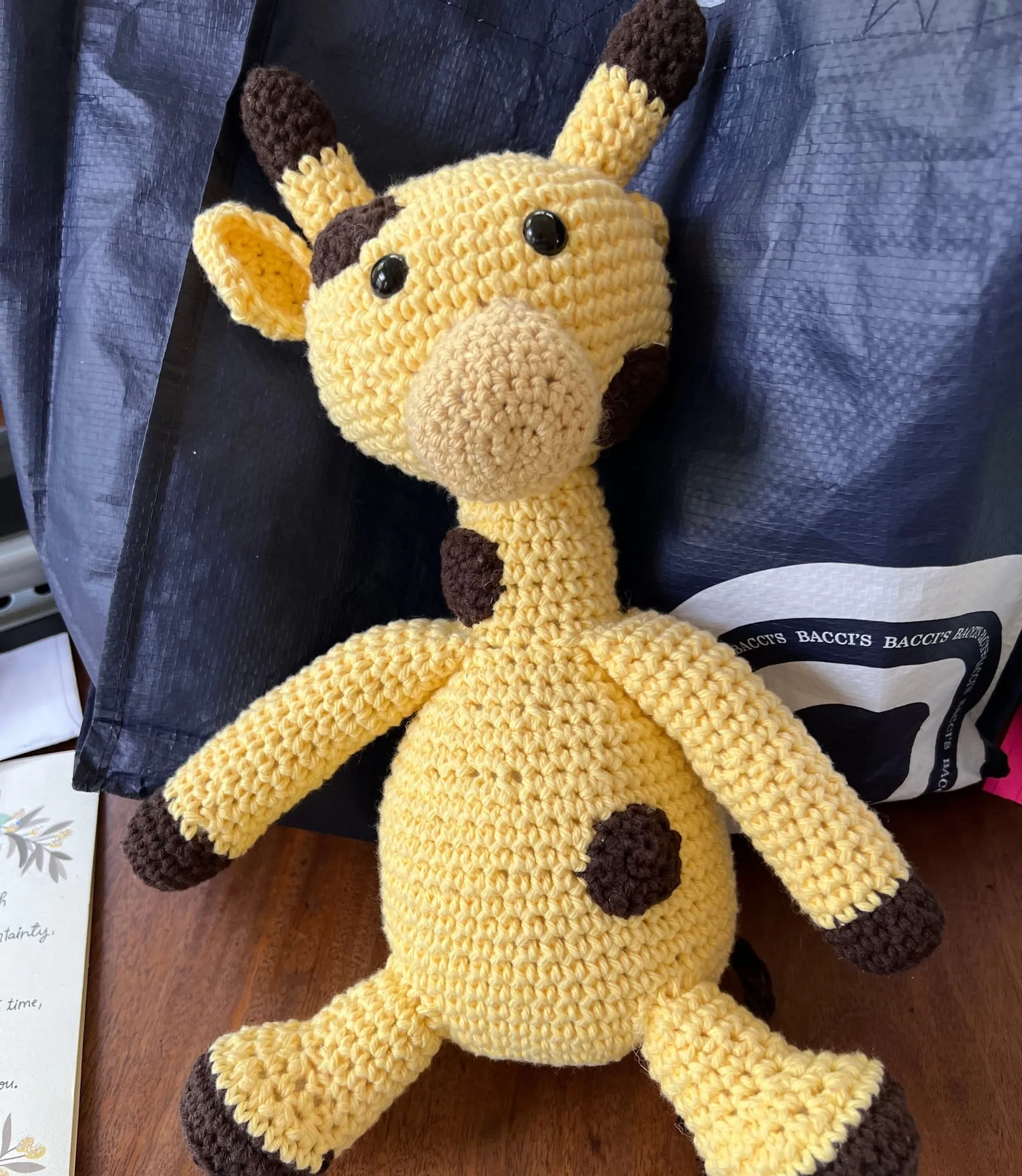 A crocheted giraffe sitting upright in pale yellow, with brown horns, hooves and spots and a pale muzzle.