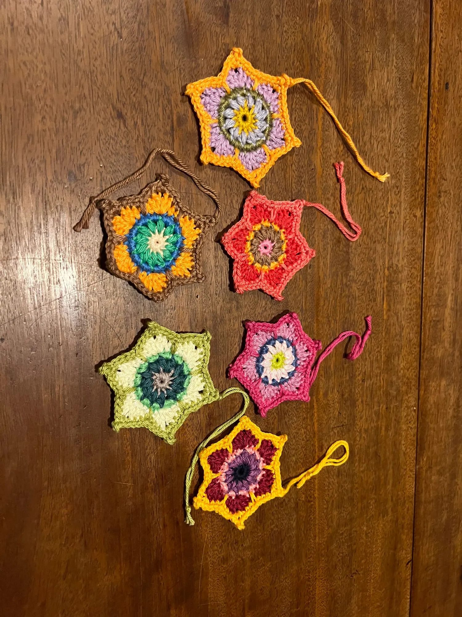 Crocheted star-shaped ornaments laid out on a wooden table, each with a hanging loop and worked in a different combination of colors.