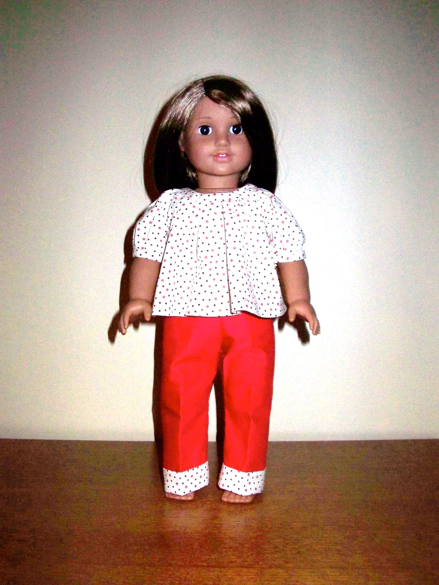 An eighteen-inch doll in a white patterned smock top and red trousers with turned-up cuffs.