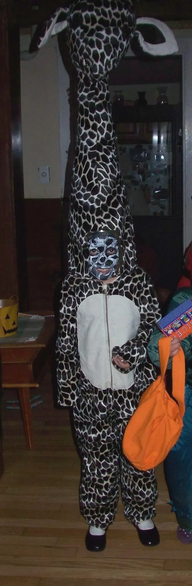 A child in a spotted giraffe costume with a face painted in matching markings, the costume's long padded neck and head standing well above their own.