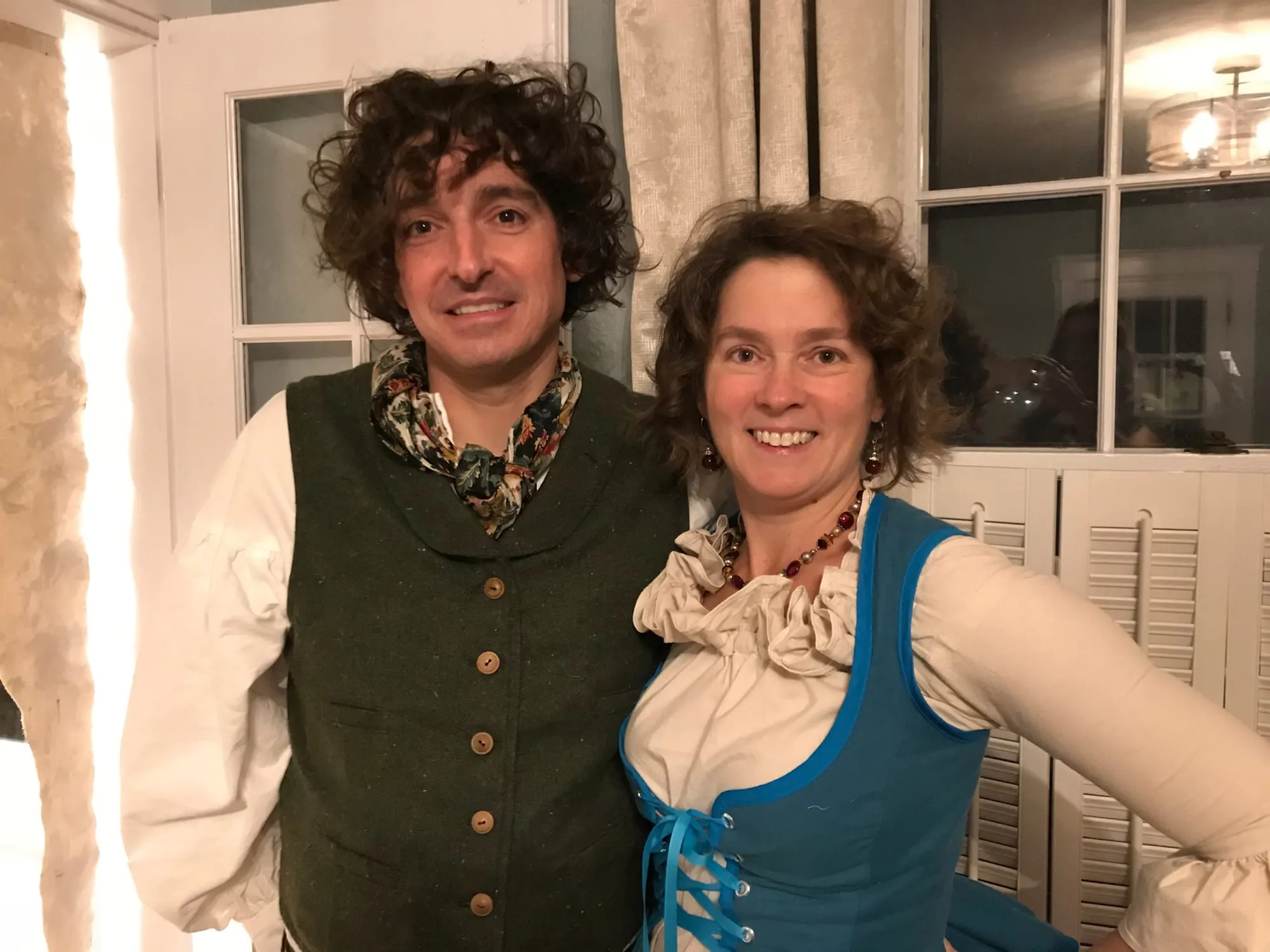 Two adults in hobbit costumes, a tailored green wool waistcoat with wooden buttons over a full-sleeved cream shirt, and a bright blue laced bodice over a ruffled blouse.