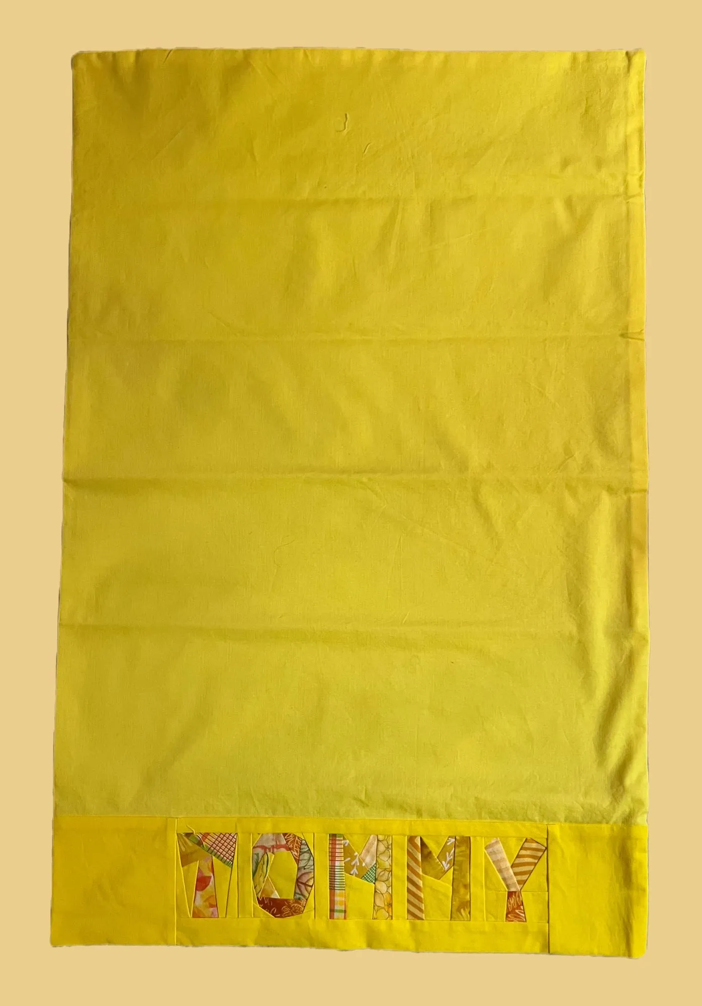 A yellow pillowcase with TOMMY across the band, each letter pieced from a different patterned yellow and orange fabric.