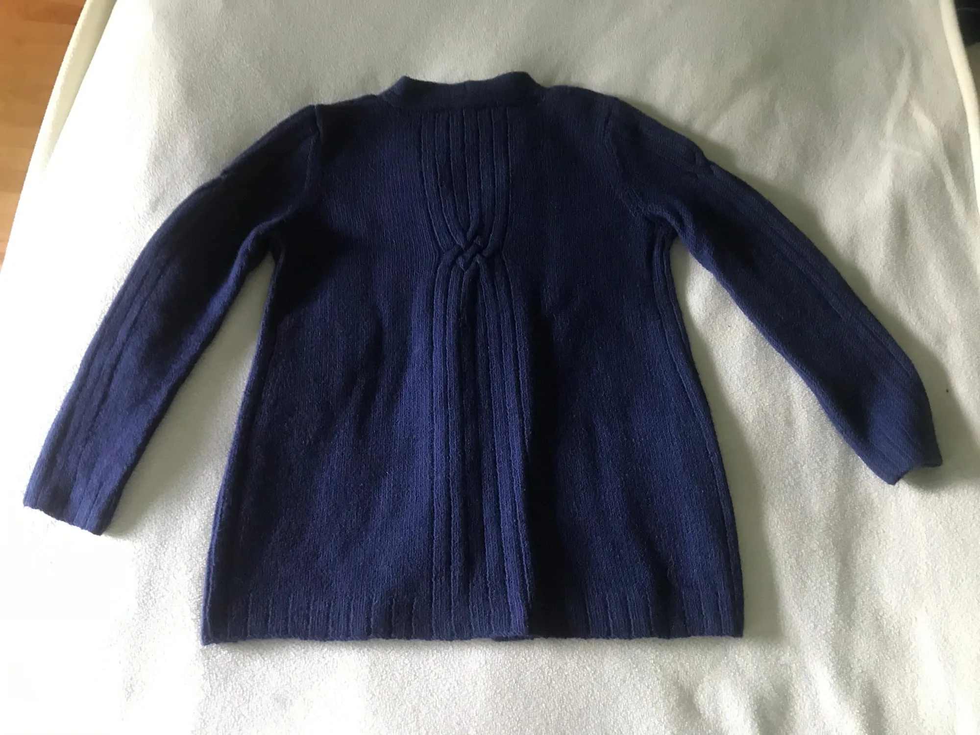 The same sweater seen from the back, laid flat on a white ground, with a plain high neckline and a ribbed panel running down the center.