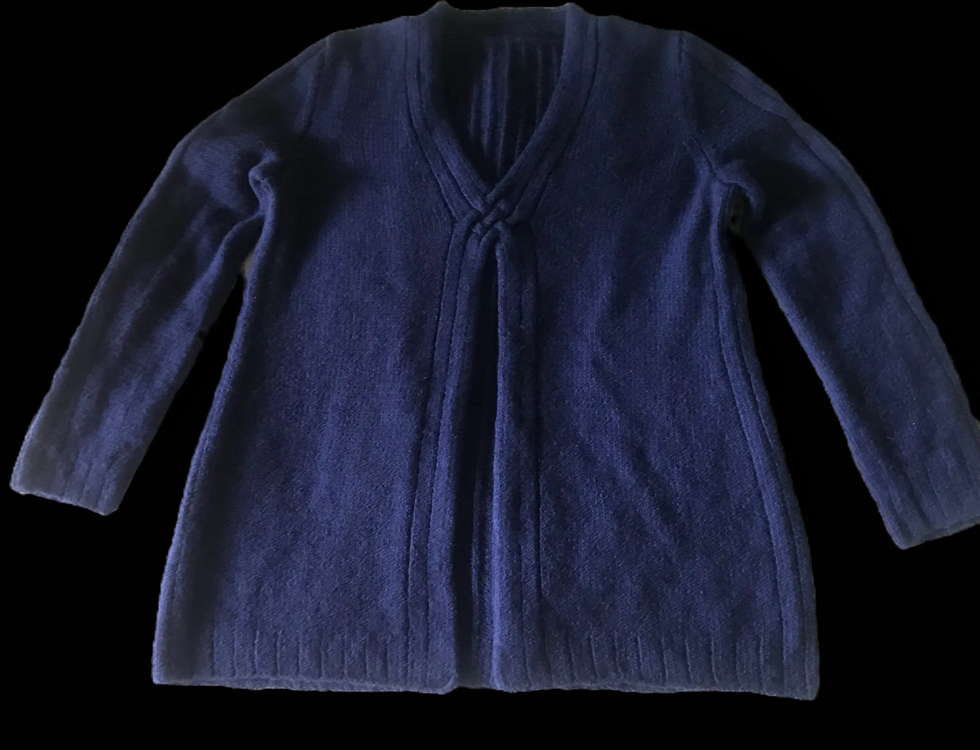 A navy sweater laid flat against a dark ground, seen from the front, opening down the center with a deep V neckline, long sleeves and a ribbed hem.