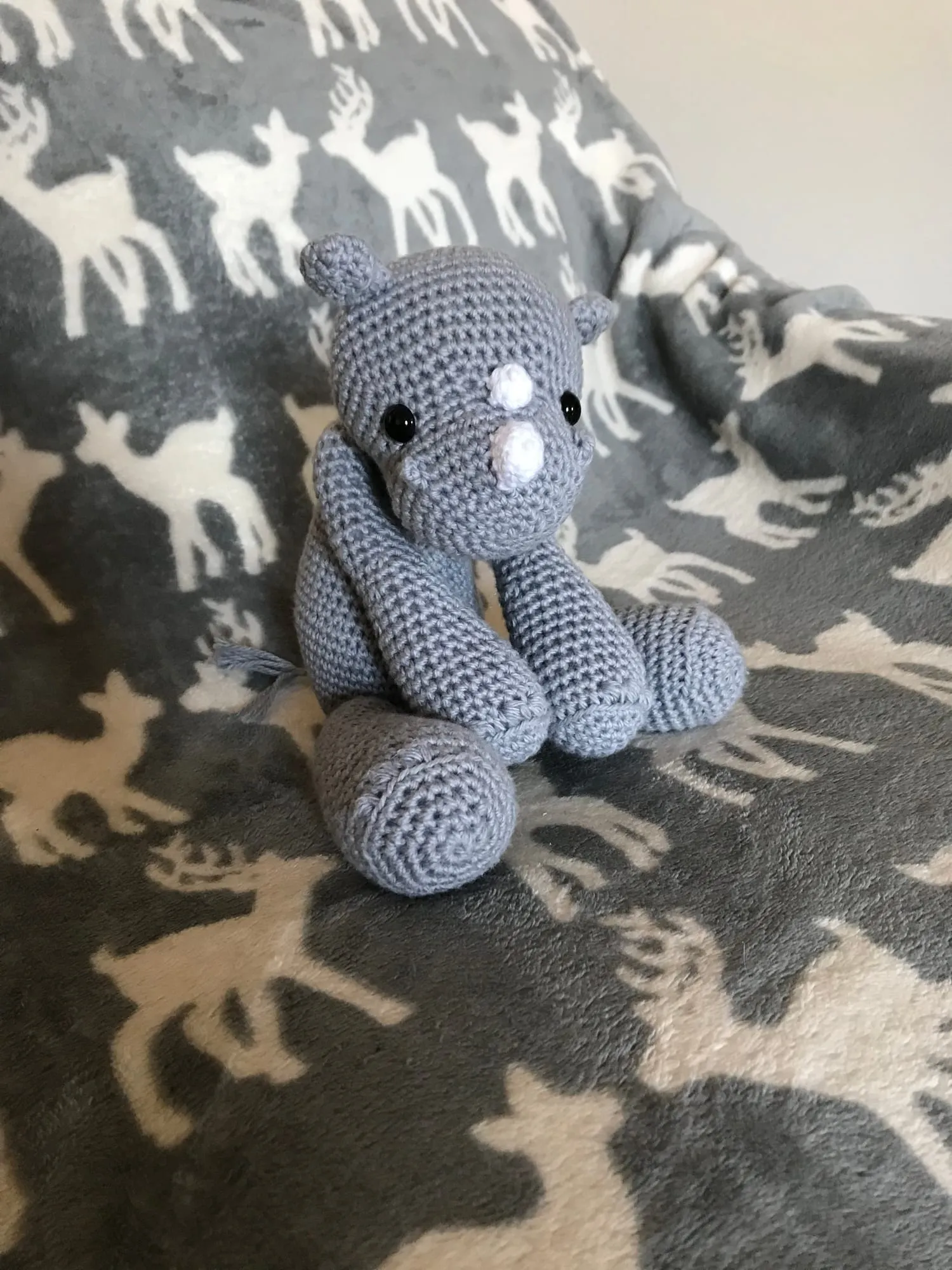 A crocheted rhinoceros in gray, sitting upright with a pale horn, small round ears and a pale belly.