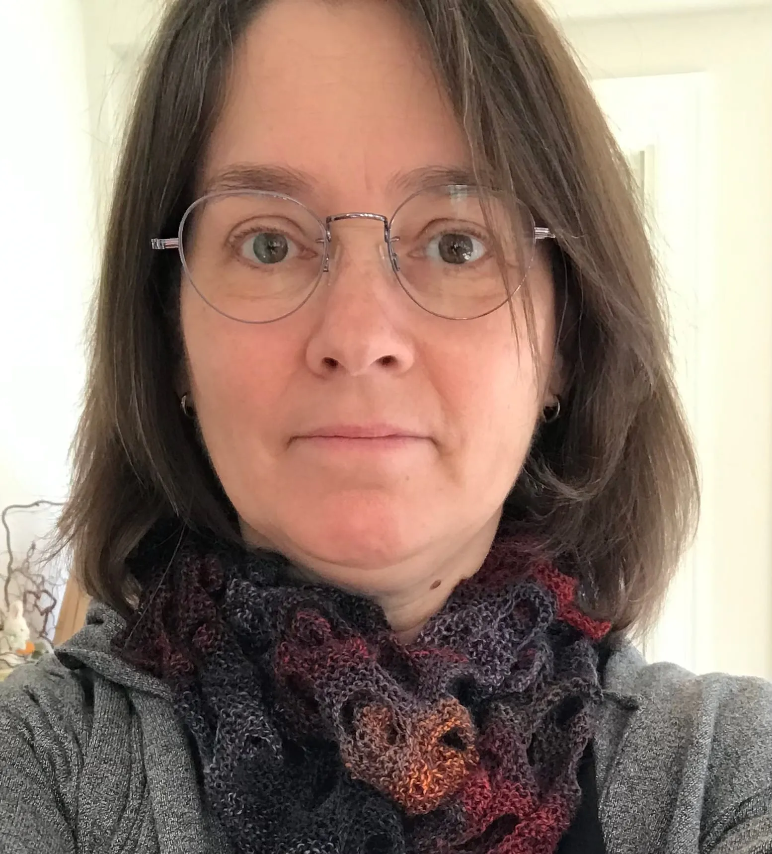 Sarah, wearing glasses and a ruffled cowl worked in dark blue, plum
           and rust.
