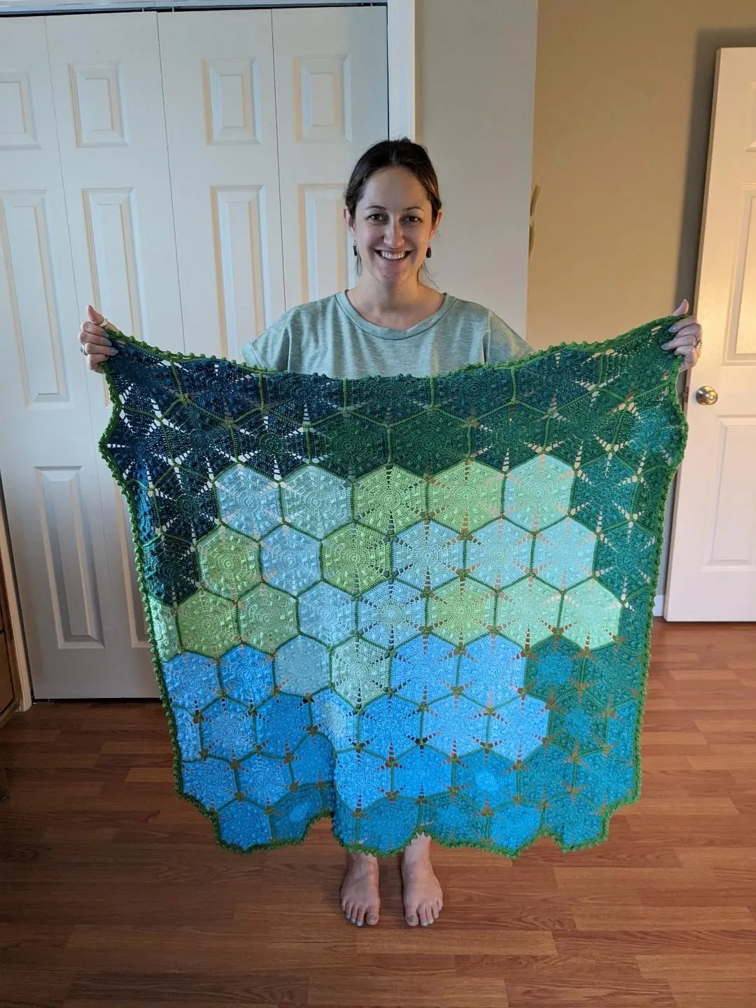 The same hexagon blanket held up open at full width, shading from deep green at the top through pale green to blue at the bottom.