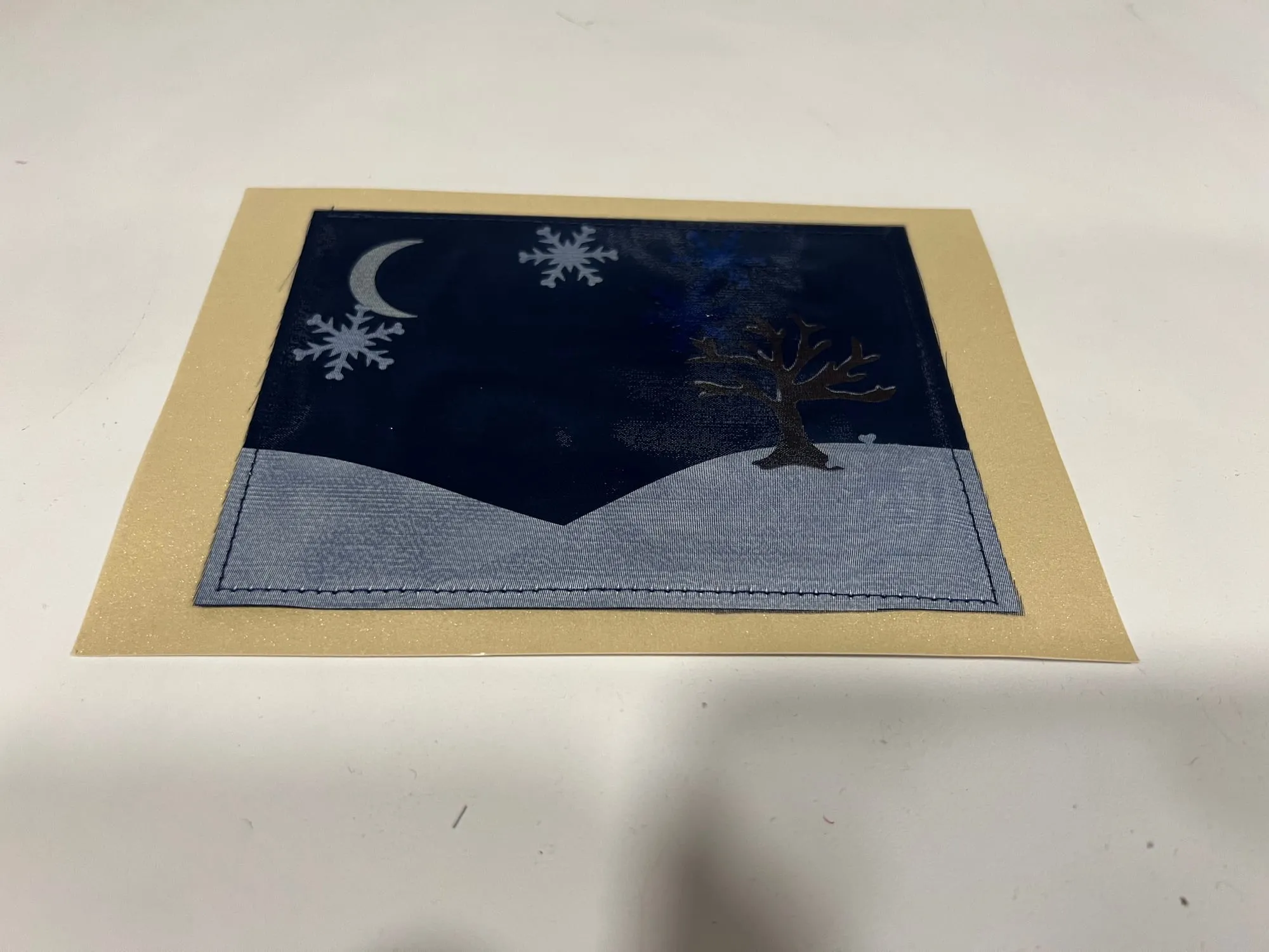 A card with a night scene panel — a crescent moon and snowflakes in a dark blue sky above a pale snowy slope with a bare tree — set in a wide cream border.