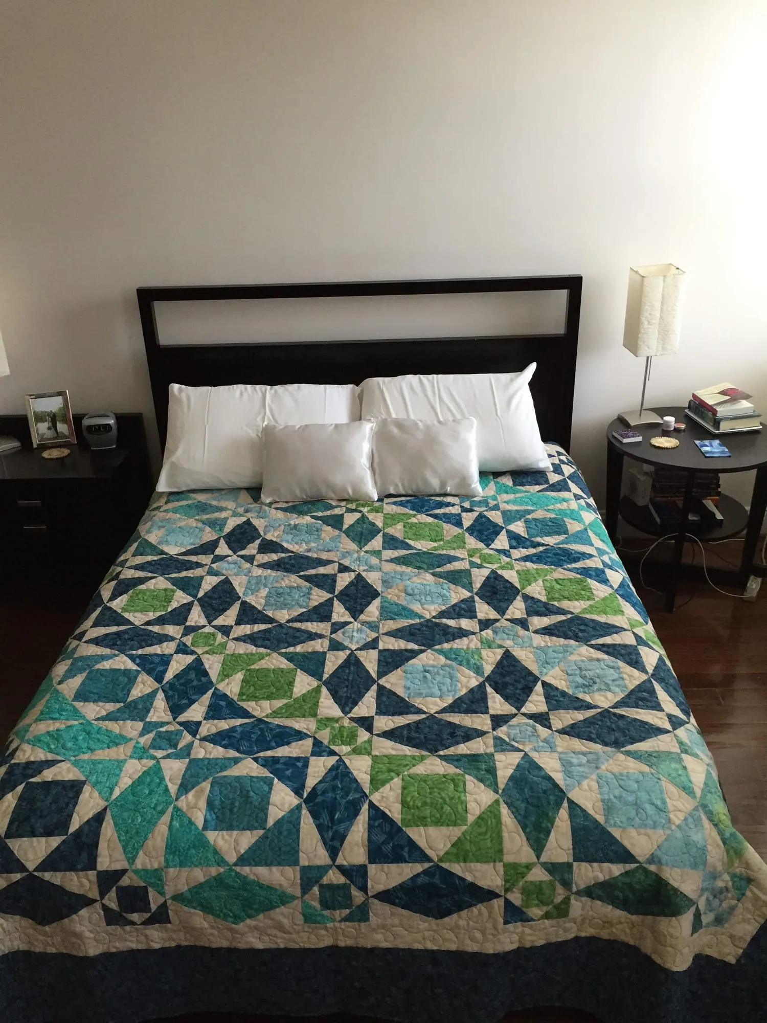 A quilt spread over a double bed whose pieced diamonds and squares create the illusion of curving waves, in greens and teals on cream.